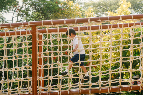 Cuadro en lienzo School-age boy climbing a rope bridge at an outdoor adventure playground in a sunny park