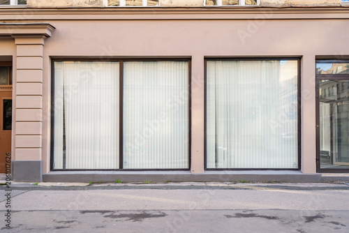 Empty commercial retail storefront mockup with closed white vertical blinds behind large glass windows on a classic urban street building facade
