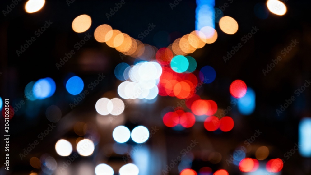 Fototapeta premium Cars move along a busy urban road, their headlights and taillights blending into a vibrant dance of colors against the dark night sky, creating an enchanting atmosphere.
