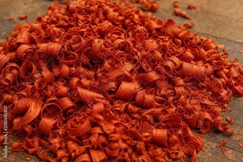 Curly, orange-red wood shavings from padauk piled on a workshop floor.
