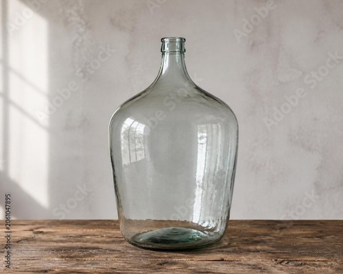 Large glass carboy on rustic wood table, home brewing storage concept.