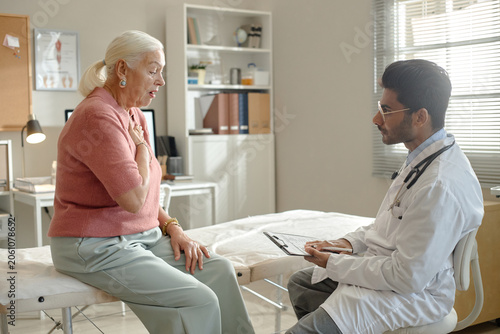 Fotografie Senior woman consulting male doctor in clinic, describing chest pain during medical visit and receiving assessment