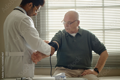Foto Senior man receiving blood pressure check from male doctor in clinic, monitoring cardiovascular health during medical visit