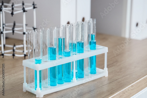 Laboratory test tubes with blue liquid in a white rack on a wooden table, sci...