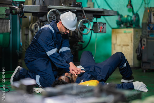 Manufacturing worker conducting chest compressions during workplace emergency drill. Industrial first aid training, accident response procedures, employee safety awareness.