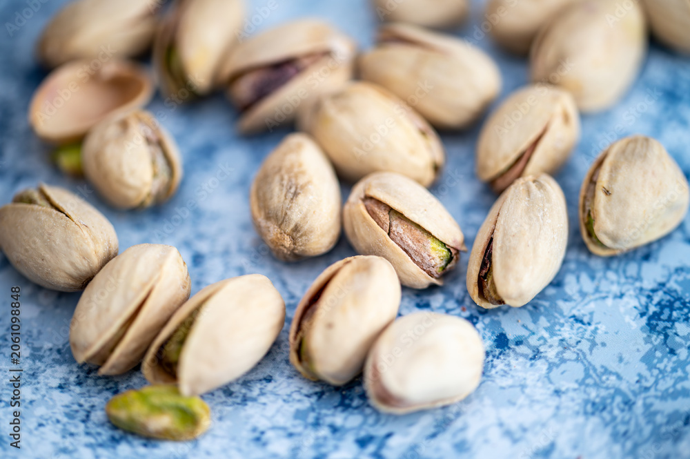 Obraz premium Macro photography of tasty pistachios in shells. Concept of healthy snacking, natural energy, and vegan protein. Close-up of roasted nuts on a vibrant blue background.