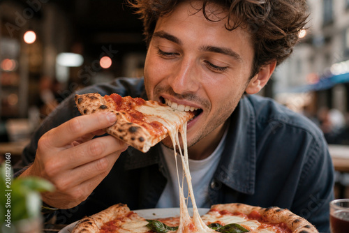 Man eating cheesy pizza slice in restaurant, joyful expression, casual dining, melted cheese pull