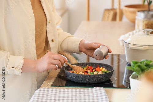 Vászonkép Woman salting fried vegetables in kitchen, closeup