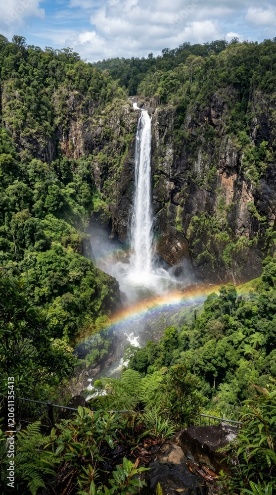 Fototapeta premium Majestic Waterfall Cascading Down Rocky Cliff with Rainbow in Lush Green Forest