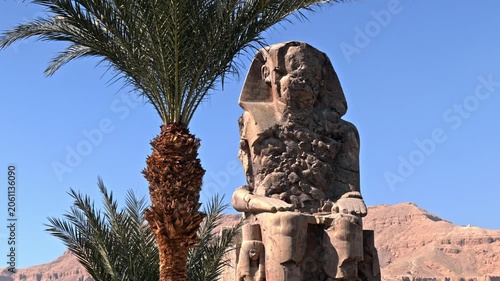 An eye-level shot capturing one of the two massive quartzite sandstone statues known as the Colossi of Memnon in Luxor, Egypt.