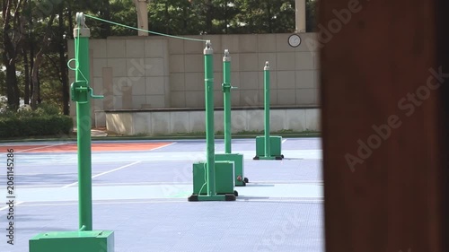 사람 스포츠 훈련 코트 야외 일상 소품 디테일 자재: 지역 공원의 한적한 야외 배드민턴 코트에 녹색 네트 지주대들이 줄지어 서 있는 풍경을 기둥 너머로 담은 동영상 클립입니다.
