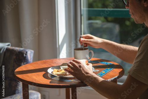 Billede på lærred Relaxed breakfast by the window, with a man enjoying coffee and toast in a sunlight morning, a calm real-life lifestyle moment