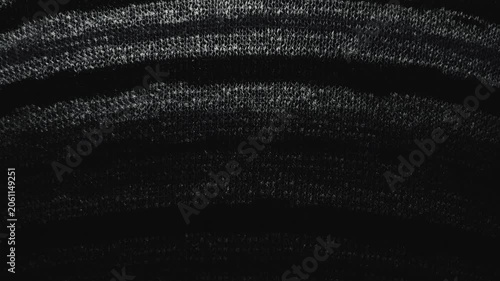 macro pan of black textured knit fabric catching moody cinematic light across curved abstract weave patterns