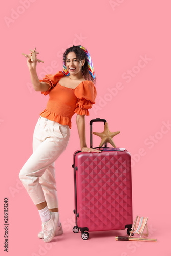 Photos Young African-American woman plying with wooden airplane near suitcases on pink