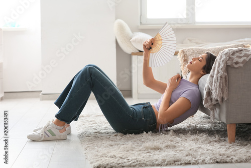 Fotografie Young pretty woman with hand fan suffering from heat and lying on floor in livin
