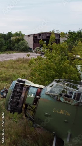 Aerial view of abandoned airplane and old helicopter on concrete near weathered hangar in greenery