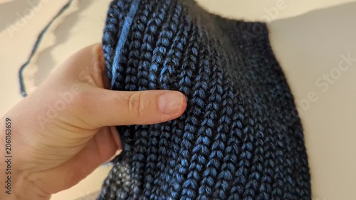 Hand gently grips a textured blue crocheted fabric. Soft fabric intricate stitch pattern and warm, tactile appeal close-up
