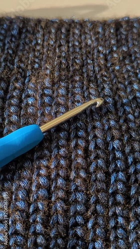 Crochet hook on dark blue textured, crochet warm chunky fabric. Close-up intricate stitch pattern and crafting detail