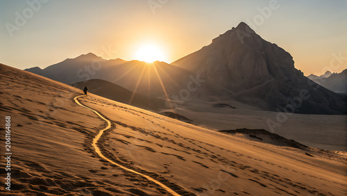 Person walking on sand dune with mountain range at sunset