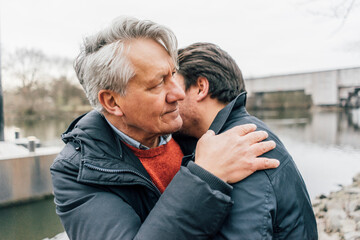 Young man and senior man embracing at the riverside