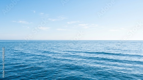 Calm blue sea water surface with gentle waves under a bright cloudy sky during a peaceful sunny day at the ocean horizon