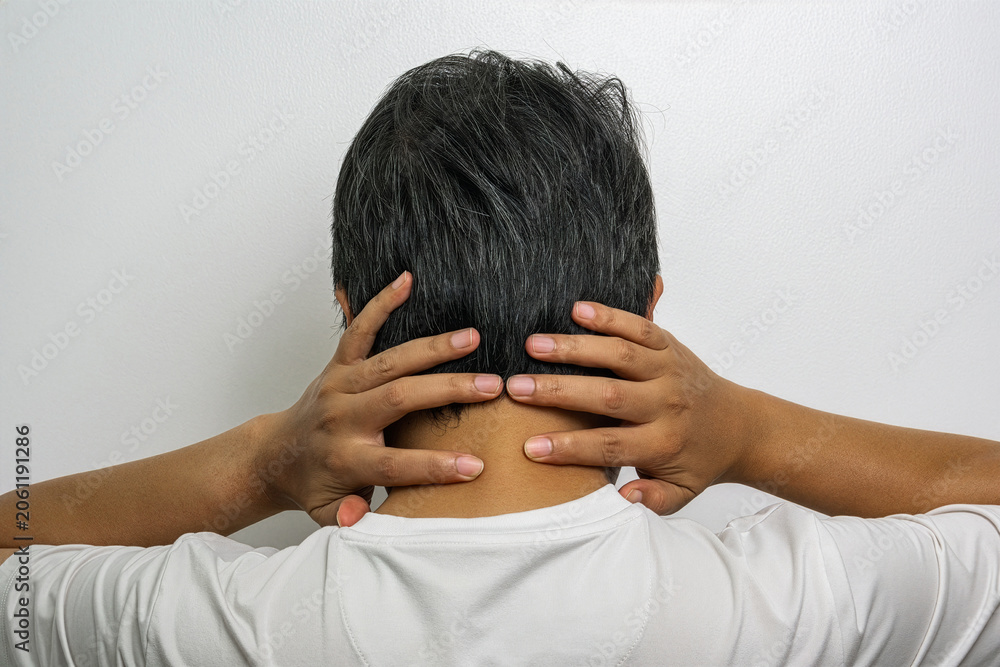 Fototapeta premium Person in white shirt holding neck with both hands, highlighted pain area, medical advertising concept for neck strain treatment.