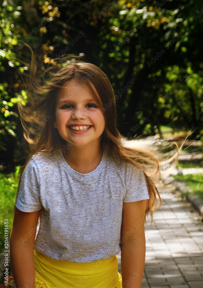 Fototapeta premium Happy girl is captured mid‑movement, laughing, with her hair gently tossed by the warm breeze, conveying a genuine sense of energy and spontaneity. Blur effect emphasizes motion feeling of liveliness.