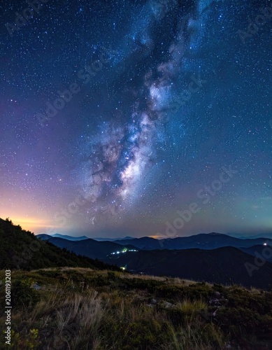 The Milky Way galaxy arcs over a mountainous landscape at night.