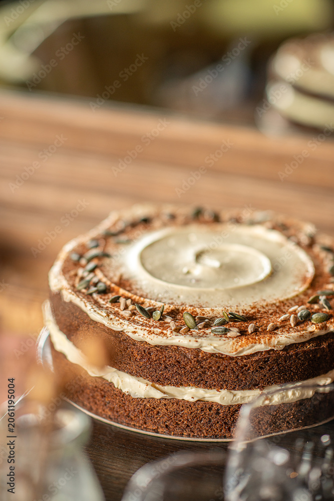 Fototapeta premium A rustic double-layer carrot cake filled and topped with cream cheese frosting, dusted with cinnamon and garnished with pumpkin seeds.