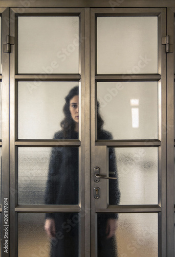 Junge Frau steht hinter einer verschlossenen Glastür – Konzept für Isolation, Barrieren, Depression und Ausgrenzung