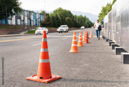 Orange traffic cones marking roadside safety zone on urban street with moving vehicles and pedestrian