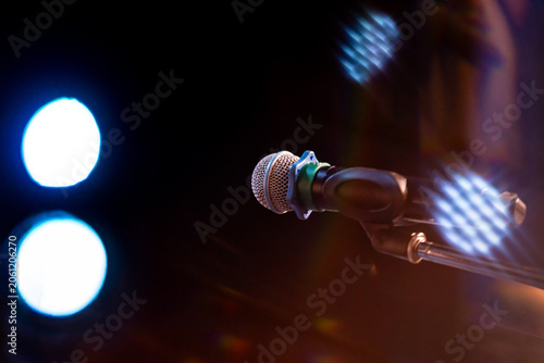 Microphone on stage stand against dark background with bright glowing spotlights. Musical equipment for concert