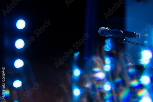 Microphone on stage with bright blue bokeh lights. Performance equipment for singer or speaker at concert.