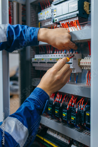 Electrician builder engineer testing and screwing equipment in fuse box and repairing of modern electricity power station using voltmeter. Automatic control cabinet