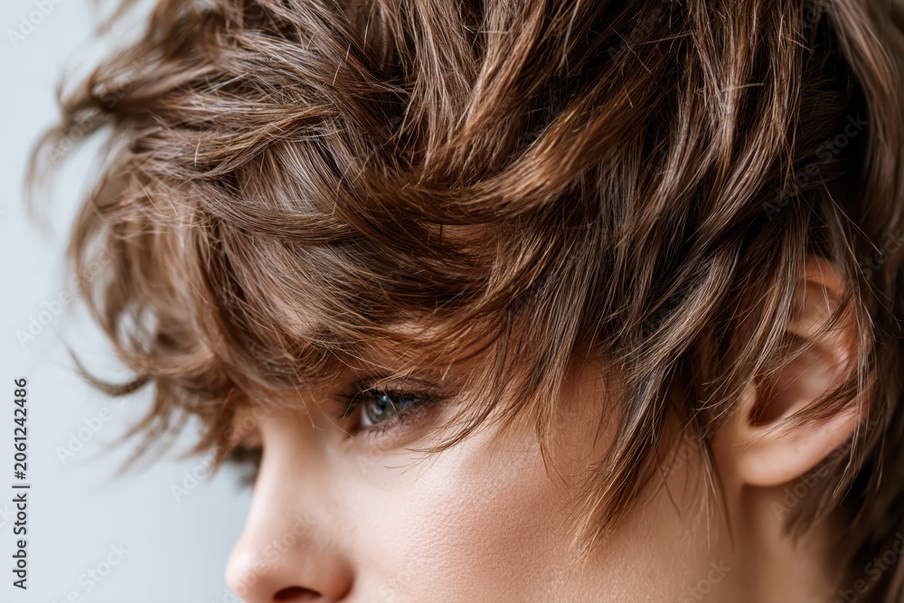 Naklejka premium Close-up profile of a young woman's face with tousled brown hair and a subtle, thoughtful expression.