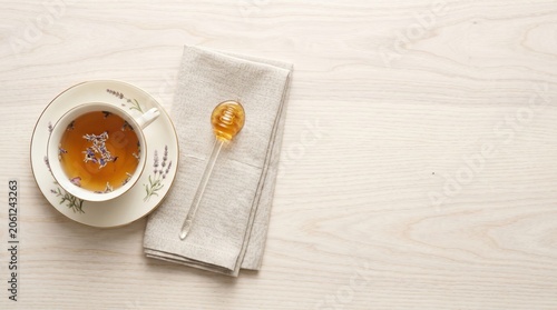 A warm cup of floral tea sits on a charming saucer beside a neat linen napkin. A honey spoon glistens invitingly, perfect for sweetening the drink during a calming afternoon.