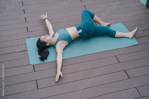 Foto Young woman lying on a yoga mat, doing a supine spinal twist to stretch her back