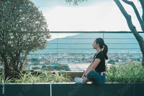 Obraz na plátně Young asian woman sitting in a relaxing yoga pose on a rooftop garden, enjoying