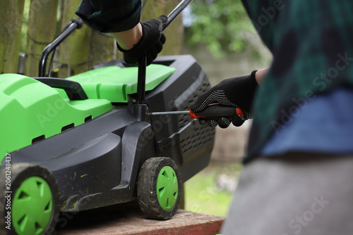 Slika na platnu Men's hands in work gloves repair a lawn mower with a screwdriver in the yard