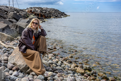 Woman relaxing on rocky shoreline beside calm sea with peaceful coastal lifestyle and travel mood