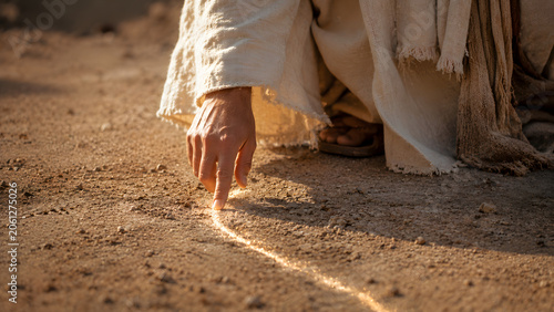 Closeup of a person in traditional robes drawing a line in the sand