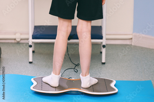 A cute boy is practicing on a balance board for children with cerebral palsy.
