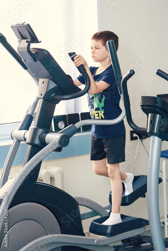 A cute boy is working out on a gym machine
