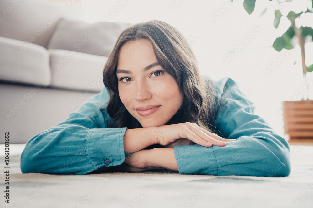 Naklejka premium Relaxed young woman portrait lying on living room floor smiling, cozy home lifestyle and natural beauty closeup