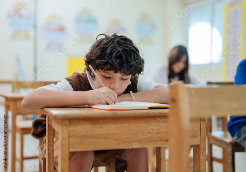 Foto Bored student boy writing in notebook while leaning on desk during school lesson