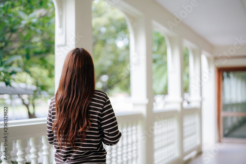 Tablou pe pânză Back view of teenage student looking out from school balcony towards trees durin