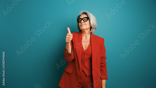 Foto Confident senior woman in a red pantsuit and glasses giving a thumbs up gesture