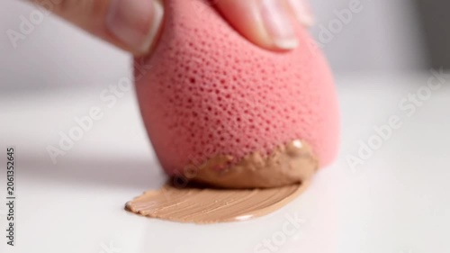 Applying cosmetic liquid foundation with a pink makeup blender sponge, beauty product, skin tone matching