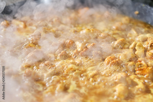 Cooking paella with chicken, vegetables, turmeric in a frying pan. Large paella pan being served outdoors. Hot Vibrant Spanish Paella. Selective focus.