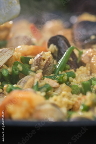 Cooking paella with chicken, seafood, and vegetables in a frying pan. Selective focus.